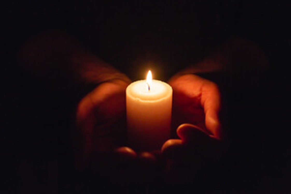 Hands holding a lit candle against darkness